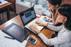 two women looking at graohic design on a laptop