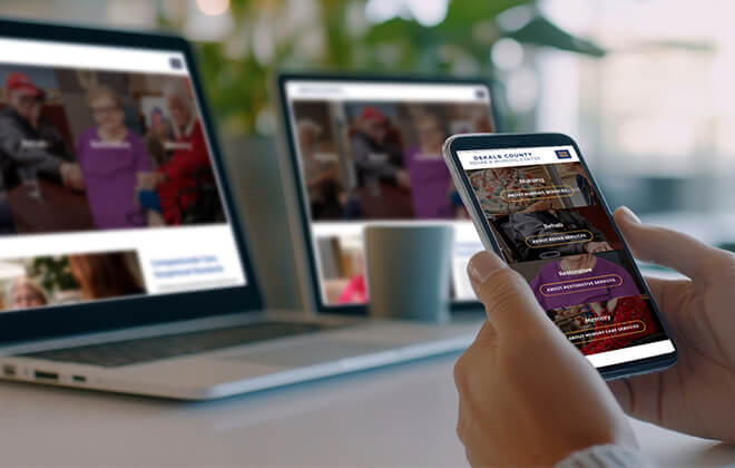 phone with dekalb county retirement community website on screen, laptop in background is on with same background